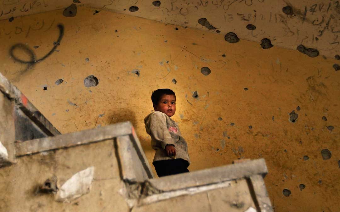 2010年10月21日，阿富汗喀布爾，一名阿富汗男孩站在充滿彈孔的牆前。攝：Chris Hondros/Getty