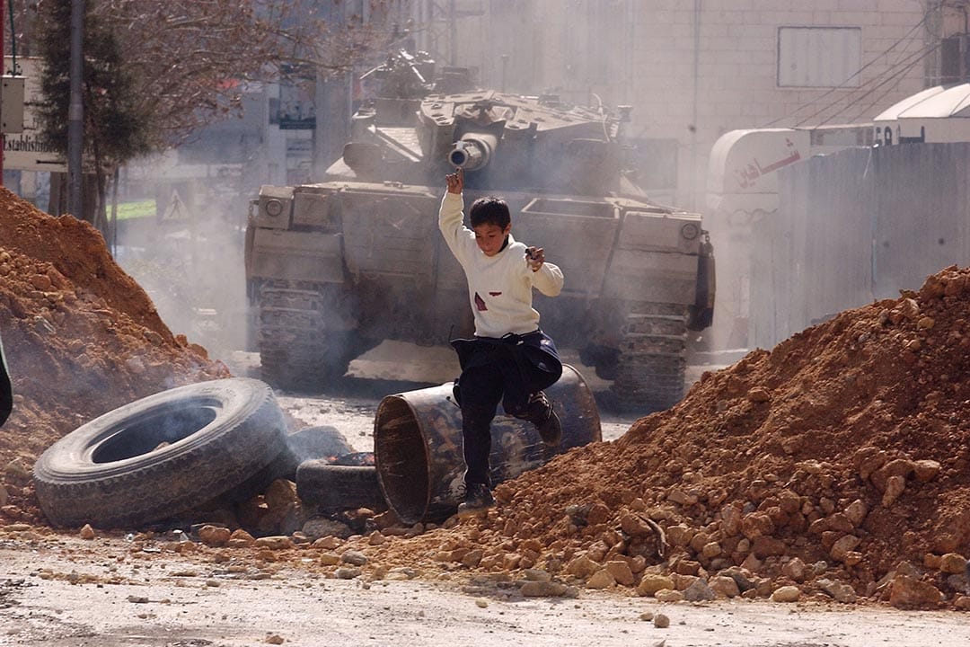 巴勒斯坦，一名男孩向坦克車投擲石頭後，逃跑尋找掩護。