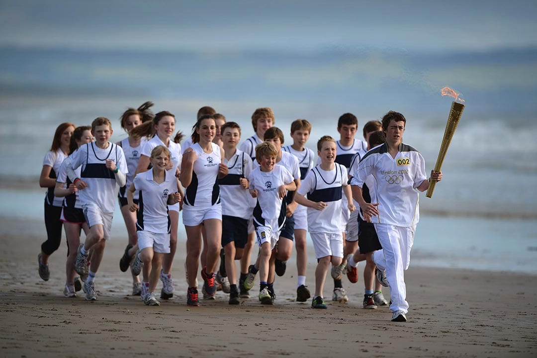 2012年6月13日，蘇格蘭，奧運火炬手Joseph Forrest帶領著馬德拉斯大學的學生沿著海灘跑步。