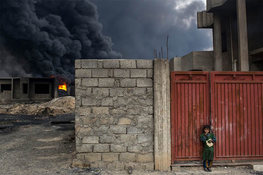 2016年11月10日,伊拉克蓋亞拉,起火的油井附近,一個女孩站在家門外吃麵包。