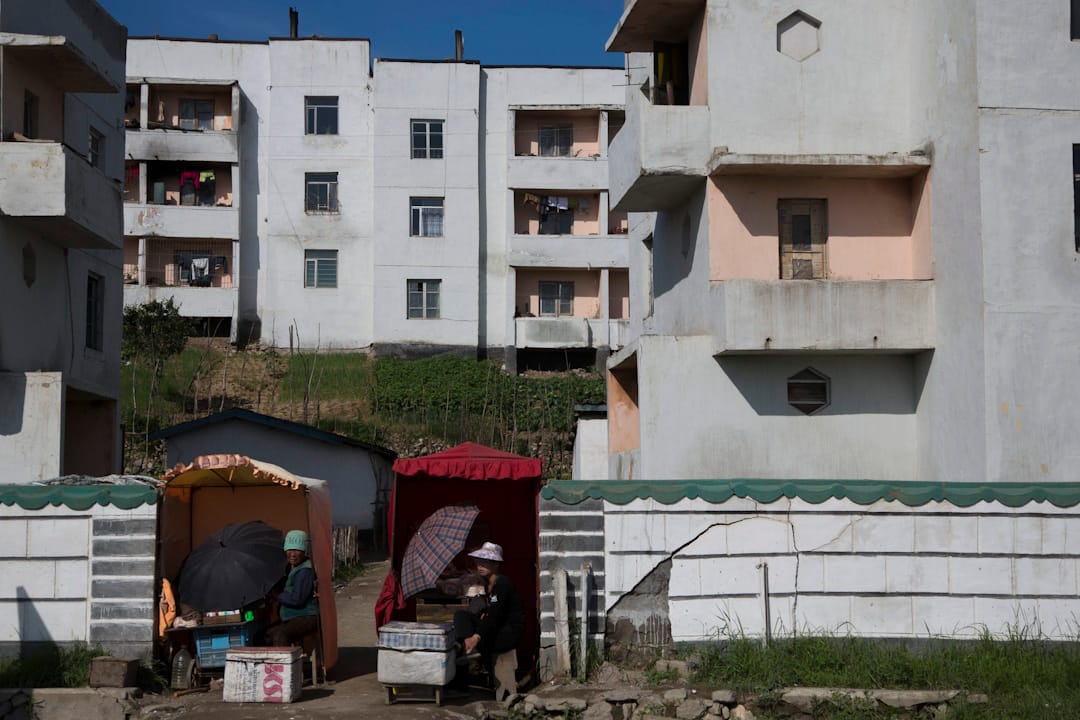清津郊区,朝鲜妇女坐在一幢住宅前的小卖车摆卖。