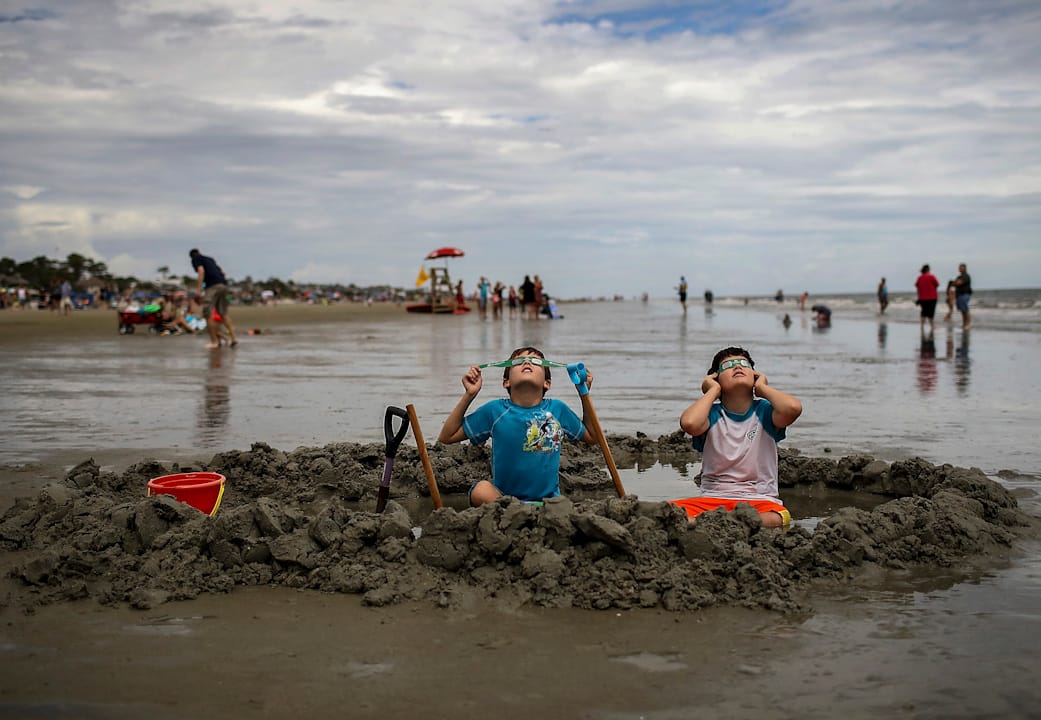 2017年8月21日，美國南卡羅來納州的希爾頓黑德島，一對兄弟坐在海灘上一邊玩泥沙一邊看日蝕。