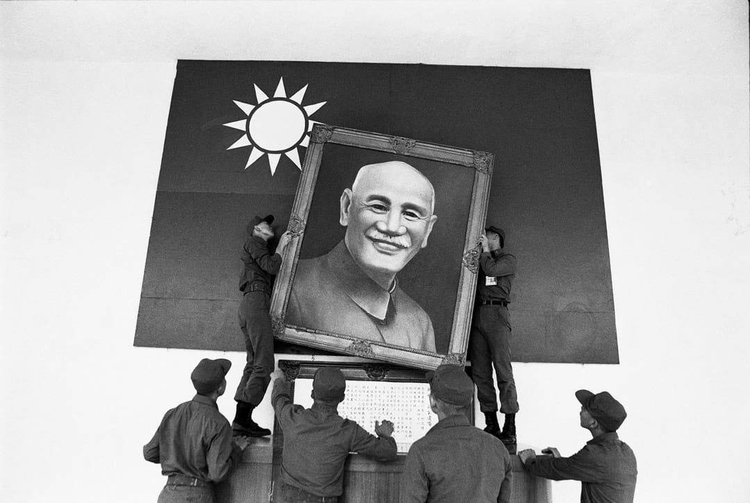 一群在佈置司令台的阿兵哥，在國旗前掛上蔣介石遺像。