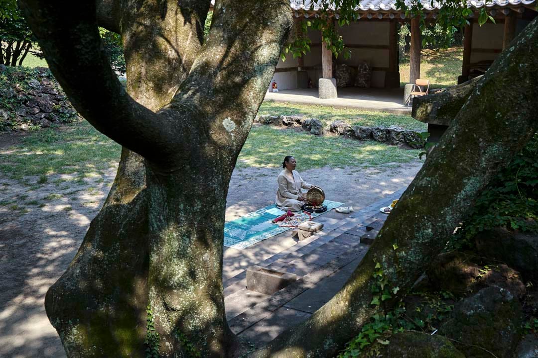 韩国济州岛,萨满巫师Dowannyeo在神树下席地祷告。