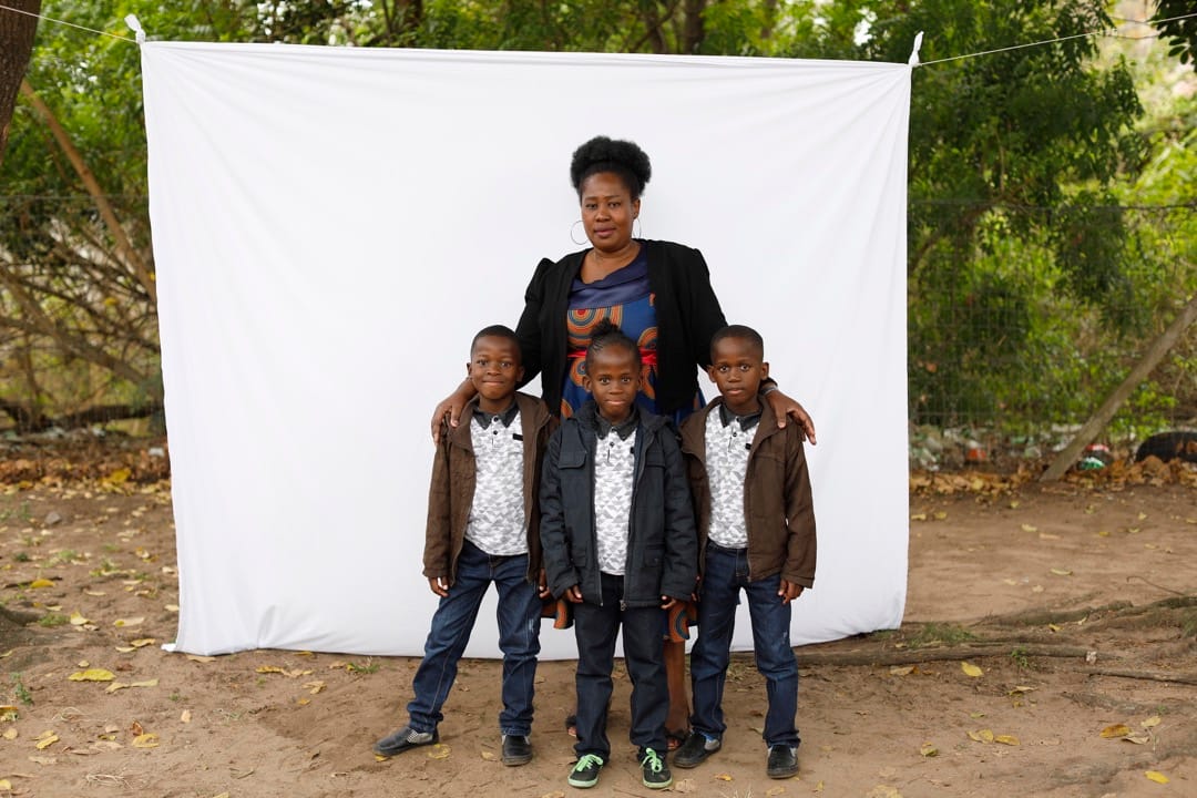 43岁的Nomathandazo Madlala和她的三胞胎儿子站在白布前。