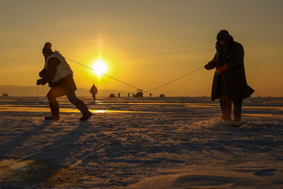 日出前,漁民扛著鋼繩向前拉。