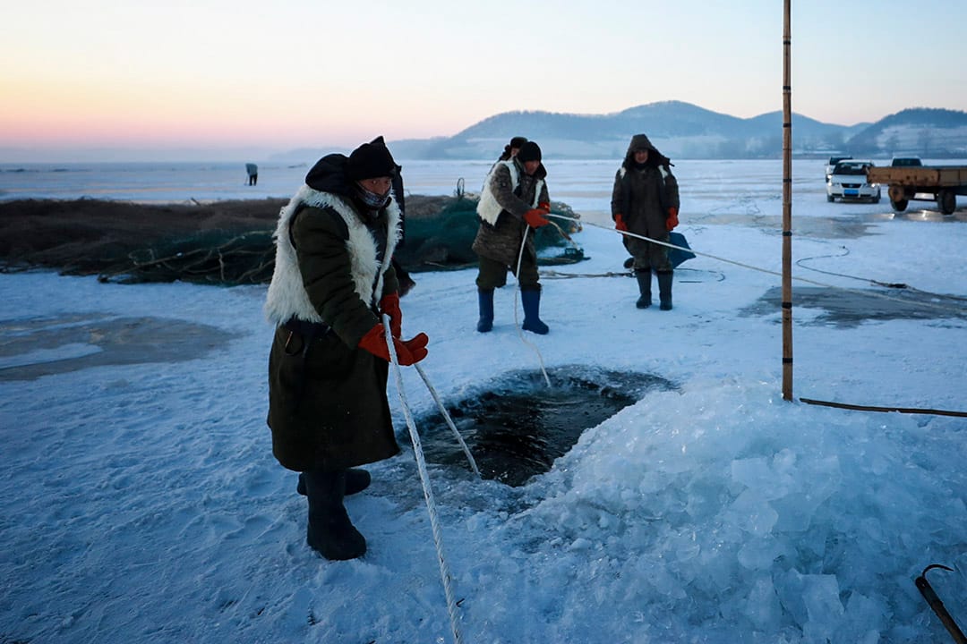 漁民在冰上鑽開一個洞,將漁網放入水中。