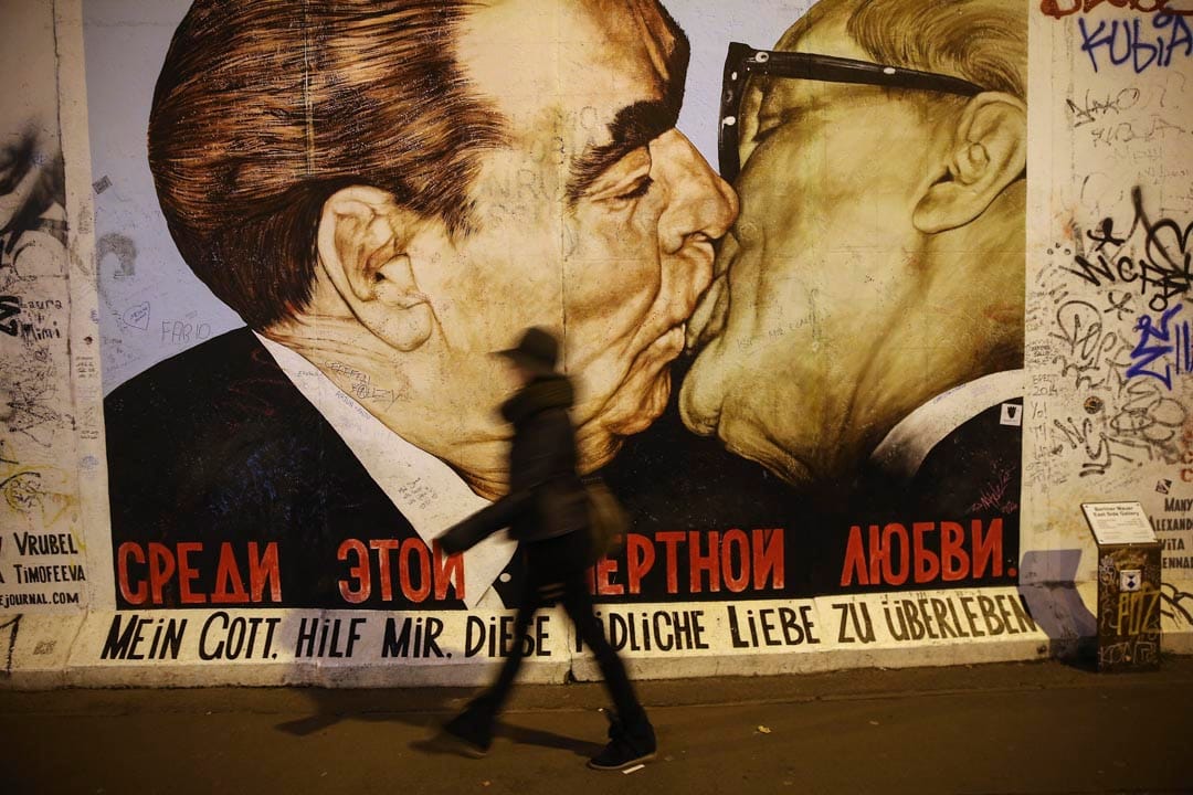 一位遊客走過一幅柏林圖牆一幅壁畫,展示前蘇聯領導人勃烈日涅夫親吻前東德共產黨領袖何內克。