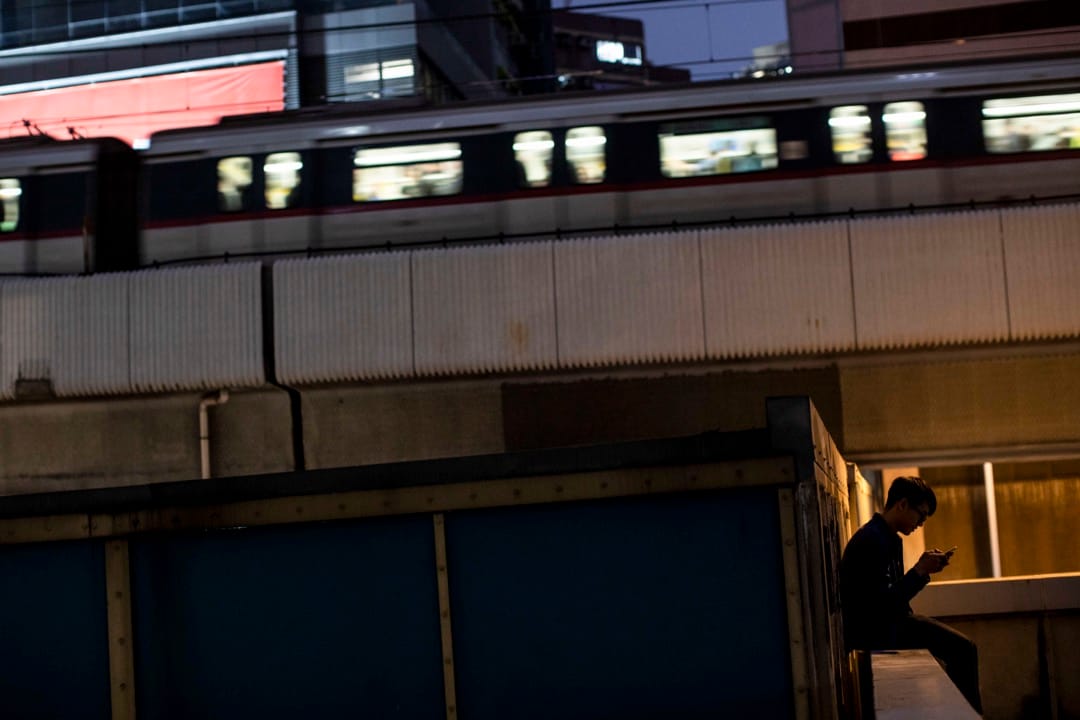 一名少年在裕民坊的平台玩手機,一列地鐵在後面的一段架空鐵路駛過。