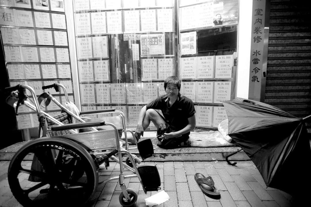 坐輪椅的發哥,因為租唔起地產舖門口廣告的4500蚊月租有電梯的劏房,他唯有瞓在地產舖門前「發個好夢」。