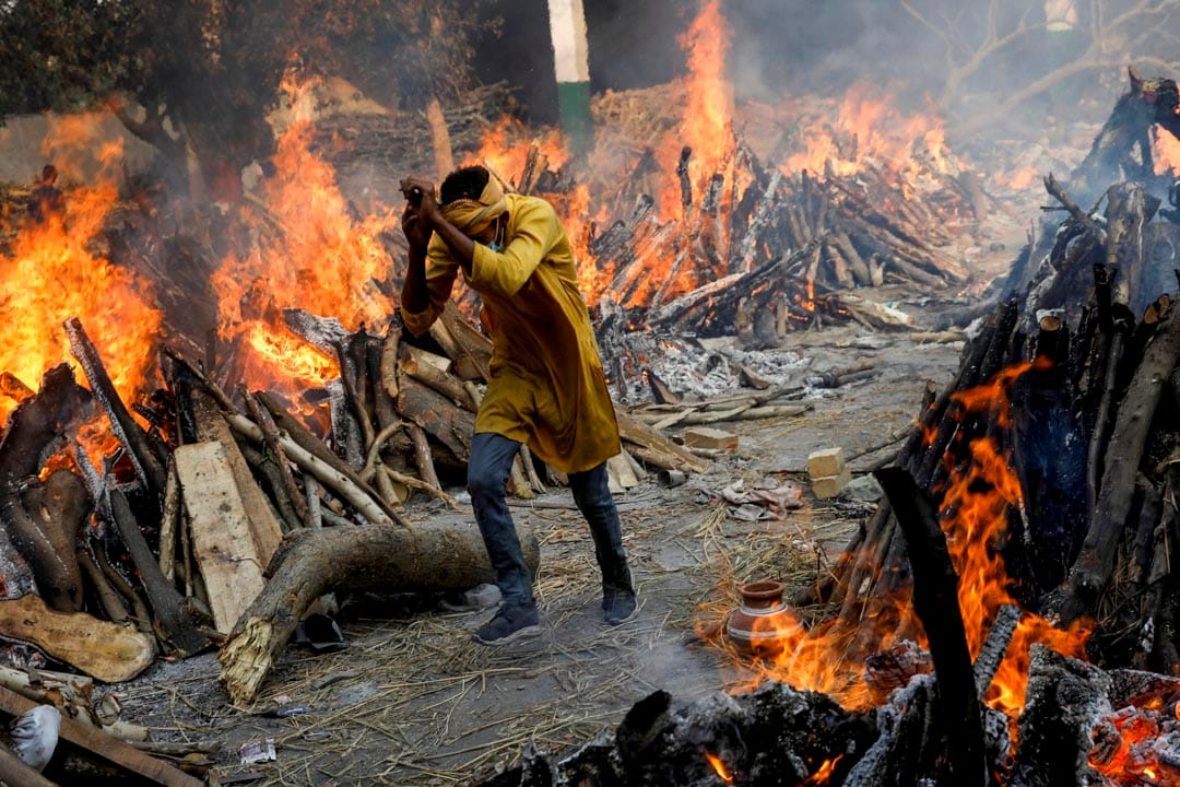 2021年4月26日，印度新德里的一個火葬場，一名男子穿過燃燒中的火堆。
