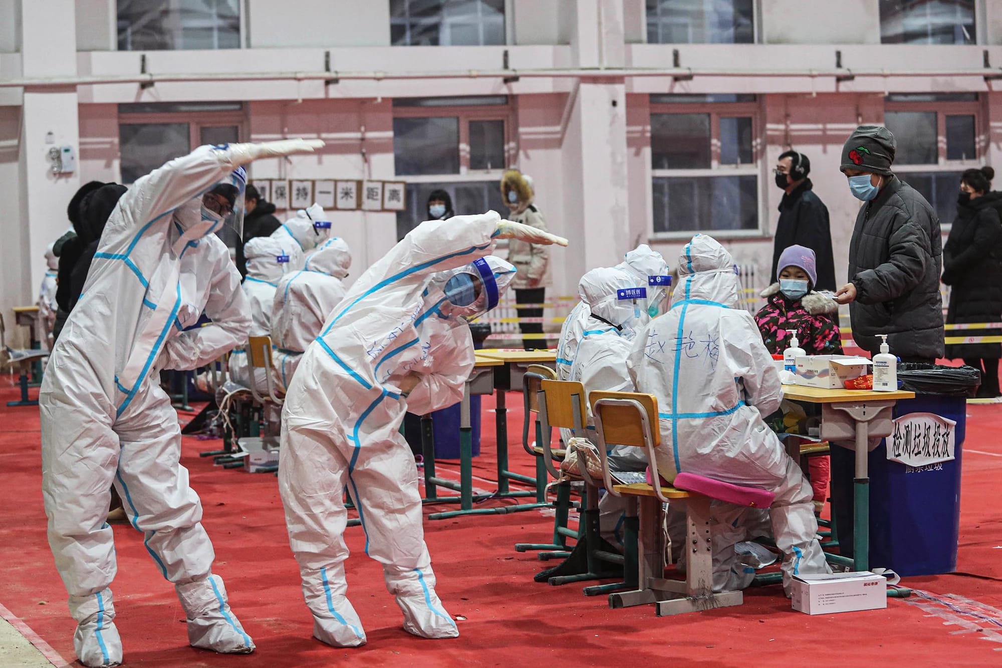 2021年1月5日中国沈阳市,身穿防护衣的医务人员在一个临时检测中心做伸展运动。