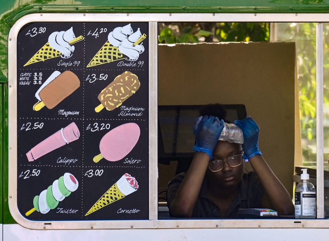 2022年7月19日,英国伦敦海德公园,一名卖雪糕的店员用冰水敷额头消暑。