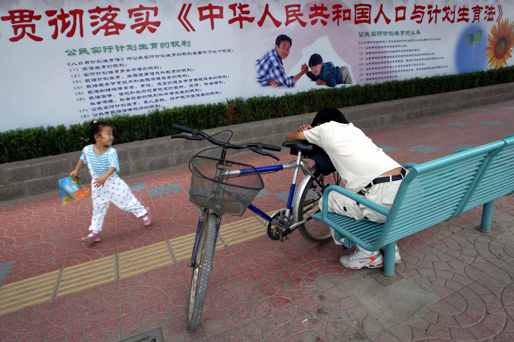 2002年8月30日,北京,一个女孩在计划生育的宣传牌前玩耍。