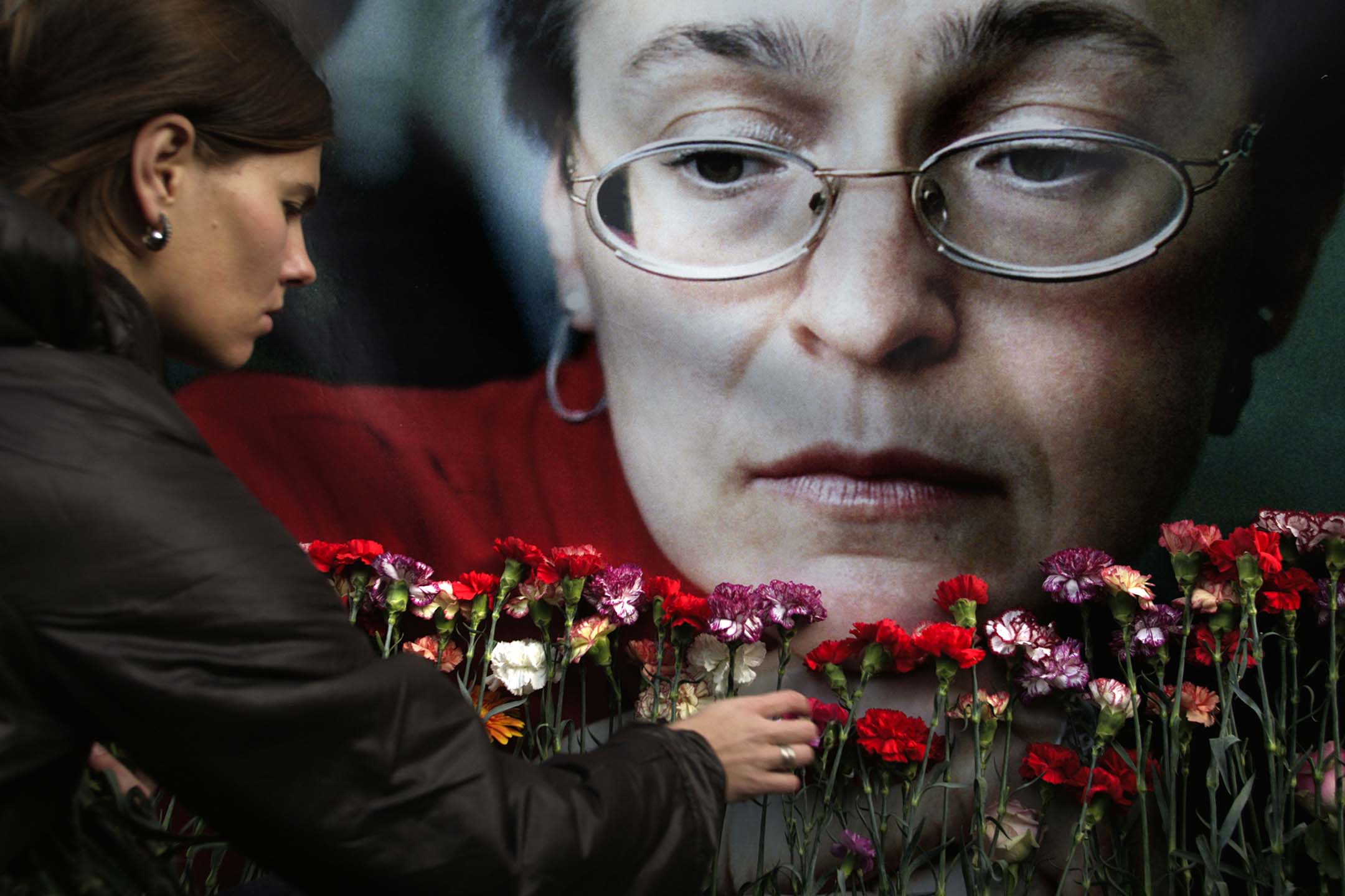 2009年10月7日,莫斯科,一名婦女將悼念的鮮花放在調查車臣戰爭罪行的《新報》(2021年諾貝爾和平獎得主)記者安娜·波利特科夫斯卡婭(Anna Politkovskaya)的肖像前。攝:Pavel Golovkin/AP/達志影像