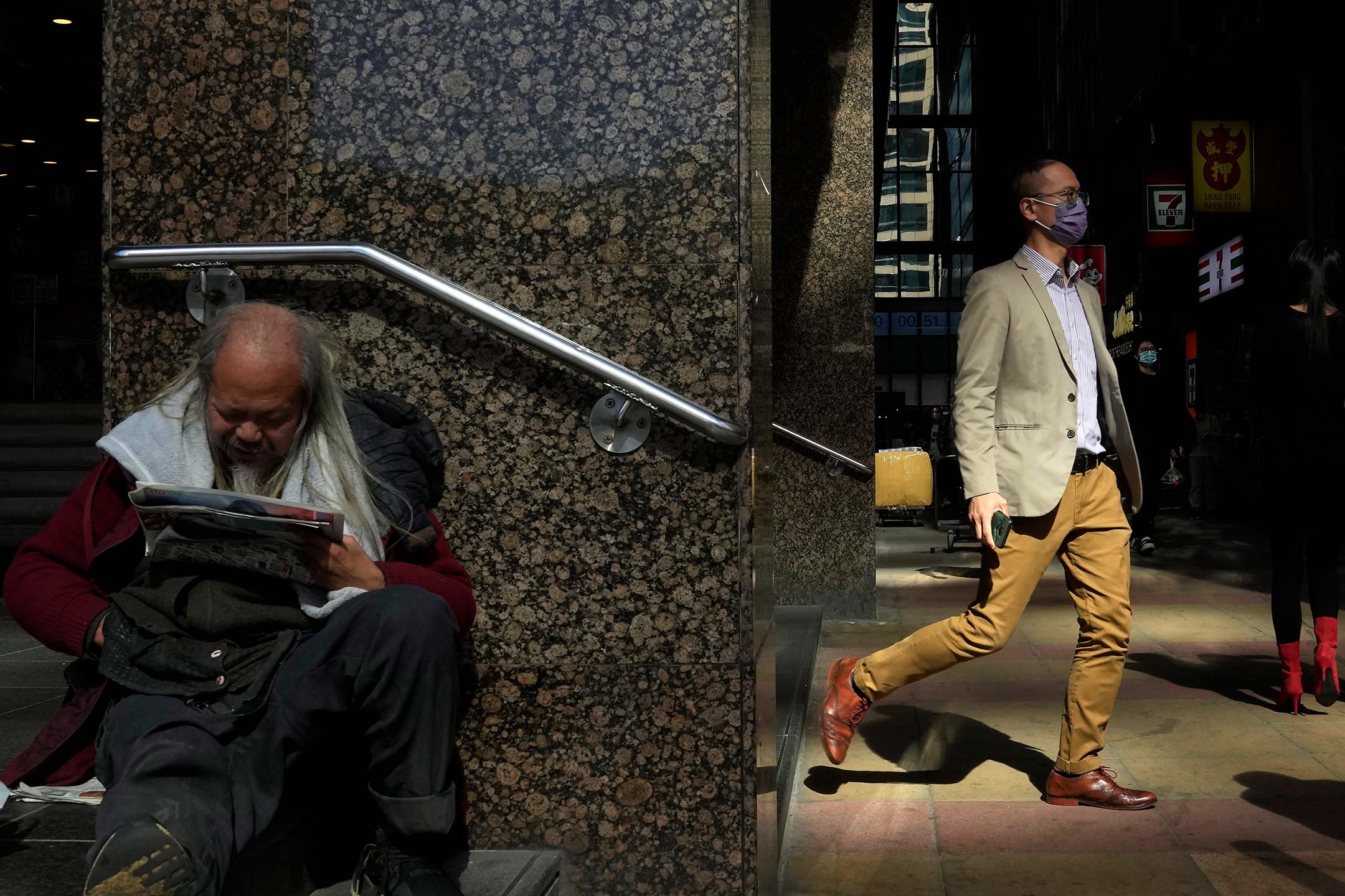 2021年12月1日,香港中環,一名男子在商業中心坐在地上看報紙。攝:Kin Cheung/AP/達志影像