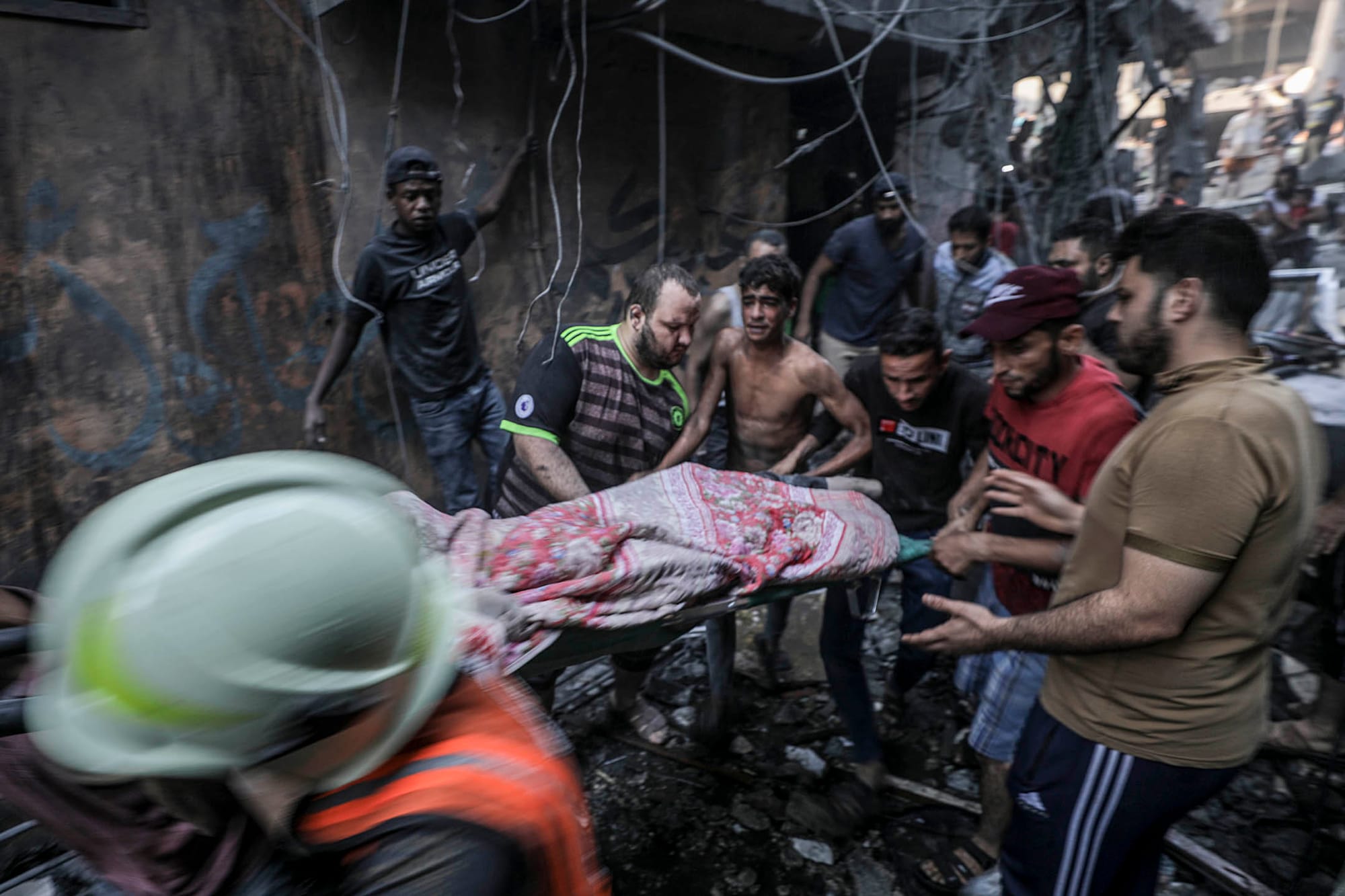 2023年10月12日,加沙走廊西部沙蒂難民營遭以色列火箭襲擊,一名傷者從現場被眾人抬出。攝:Haitham Imad/EPA/達志影像