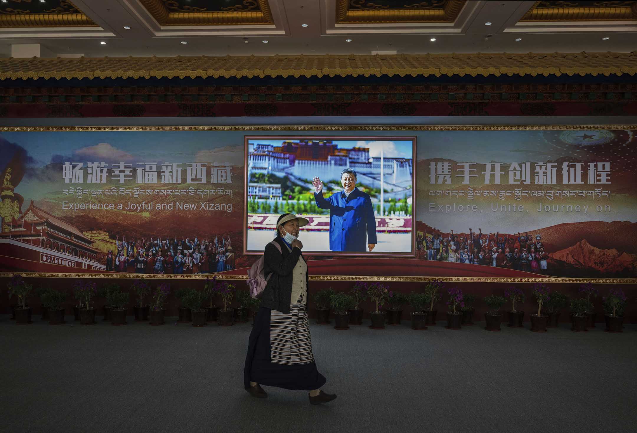 2023年6月17日,西藏拉薩,第五屆中國西藏旅遊文化博覽會的展廳裡,一名藏族婦女走過展示習近平在布達拉宮前的照片。攝:Kevin Frayer/Getty Images