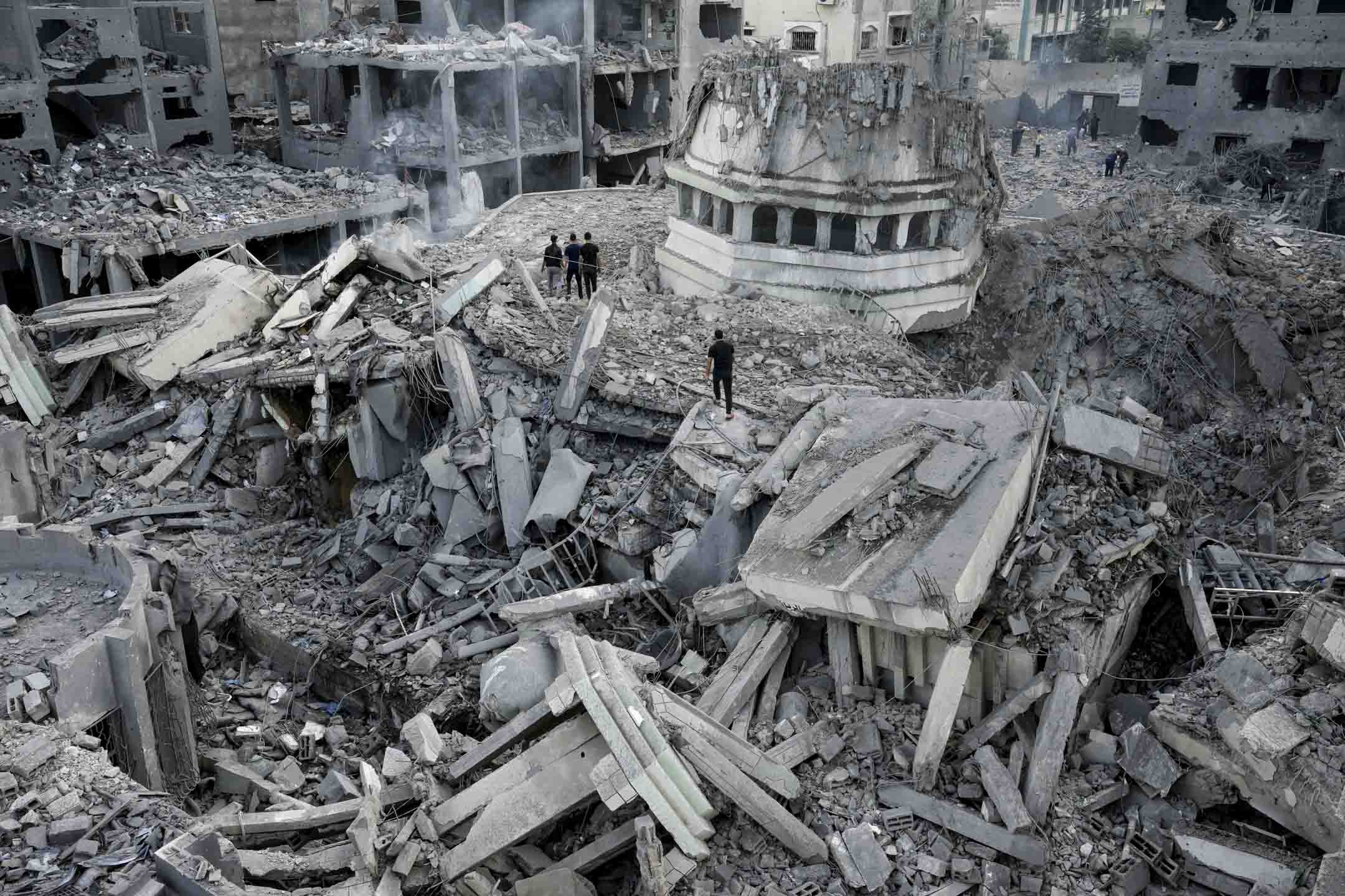 2023年10月9日清晨,以色列空襲加沙沙蒂難民營後,巴勒斯坦人檢查被摧毀的廢墟。攝:Adel Hana/AP/達志影像