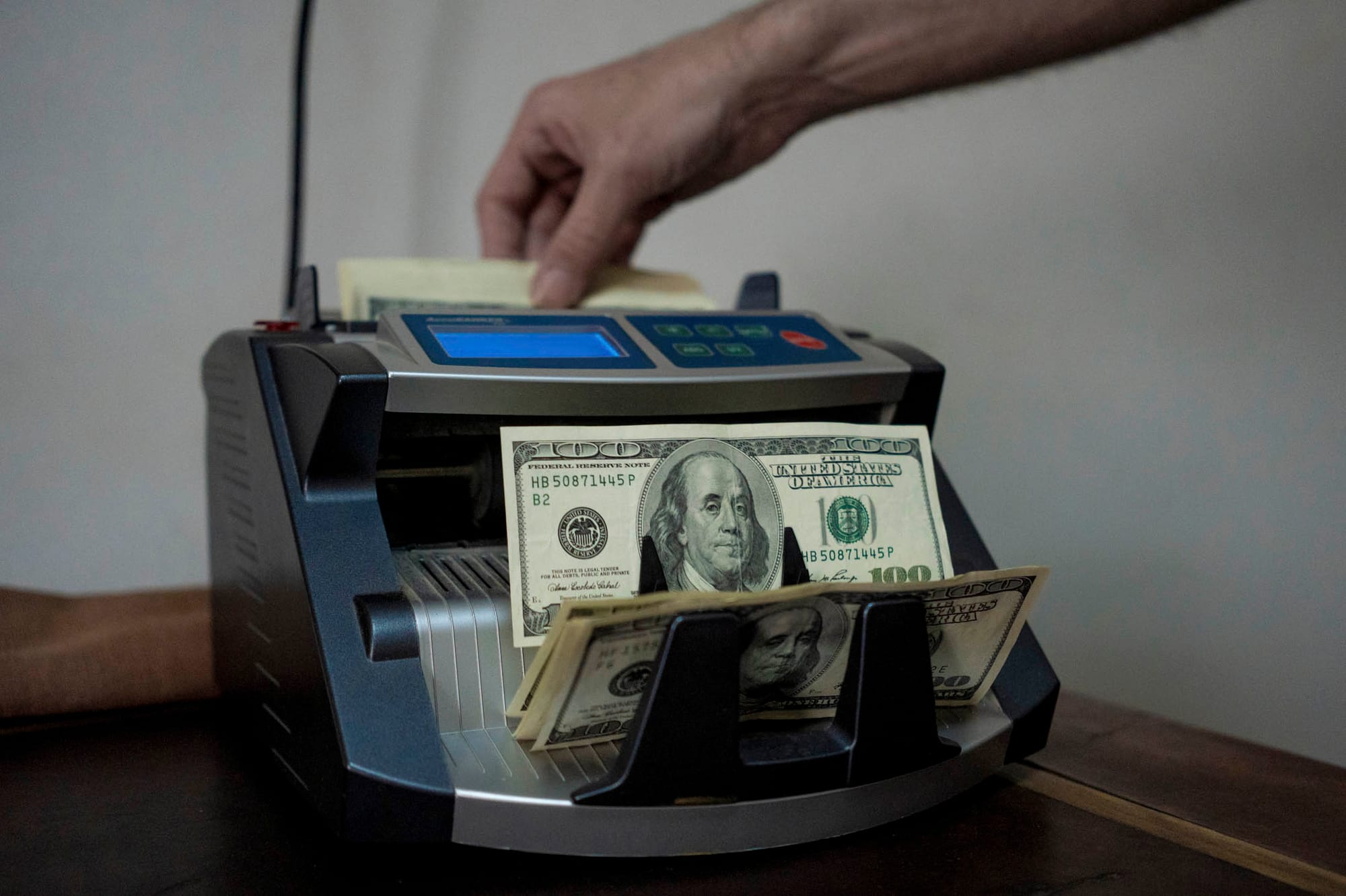 2024年1月10日,阿根廷布宜諾斯艾利斯的一家貨幣兌換所,一名工作人員使用點鈔機點鈔100美元紙幣。攝:Anita Pouchard Serra/Bloomberg via Getty Images