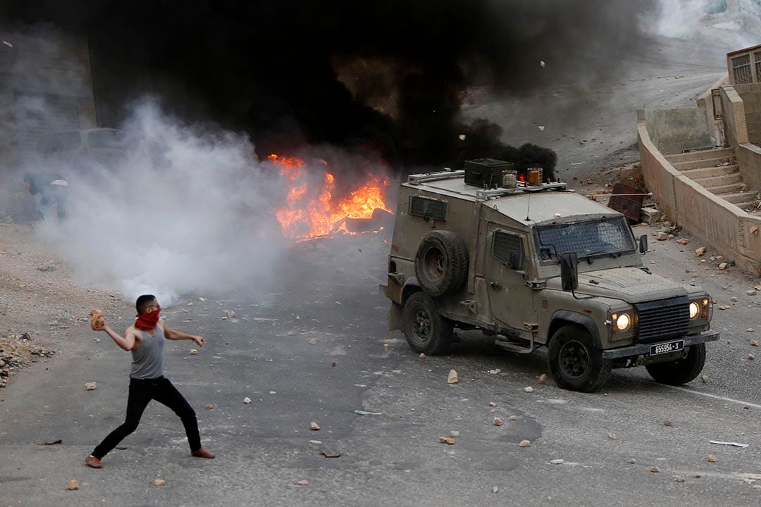 2015年10月6日，约旦河西岸，巴勒斯坦青年向以色列军车投掷石头。摄：Majdi Mohammed/AP