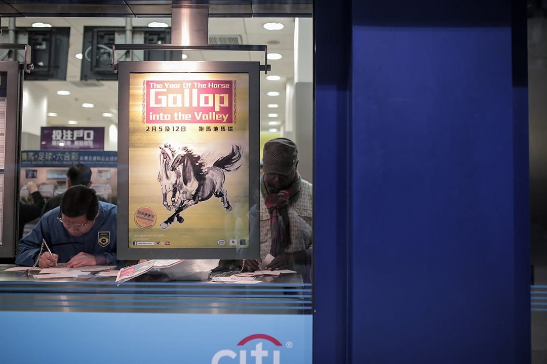 2014年，一位難民於投注站內投注。他來自剛果，因政治問題逃離剛果後輾轉來到香港，獲批確認為難民後一直未獲轉送至第三國，在香港滯留了十二年。攝: Billy H.C. Kwok/ 端傳媒