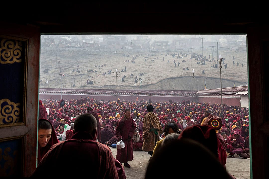 在色達喇榮五明佛學院內,一些喇嘛在喝茶,背後坐著成千的喇嘛。攝:Kevin Frayer/Getty Images