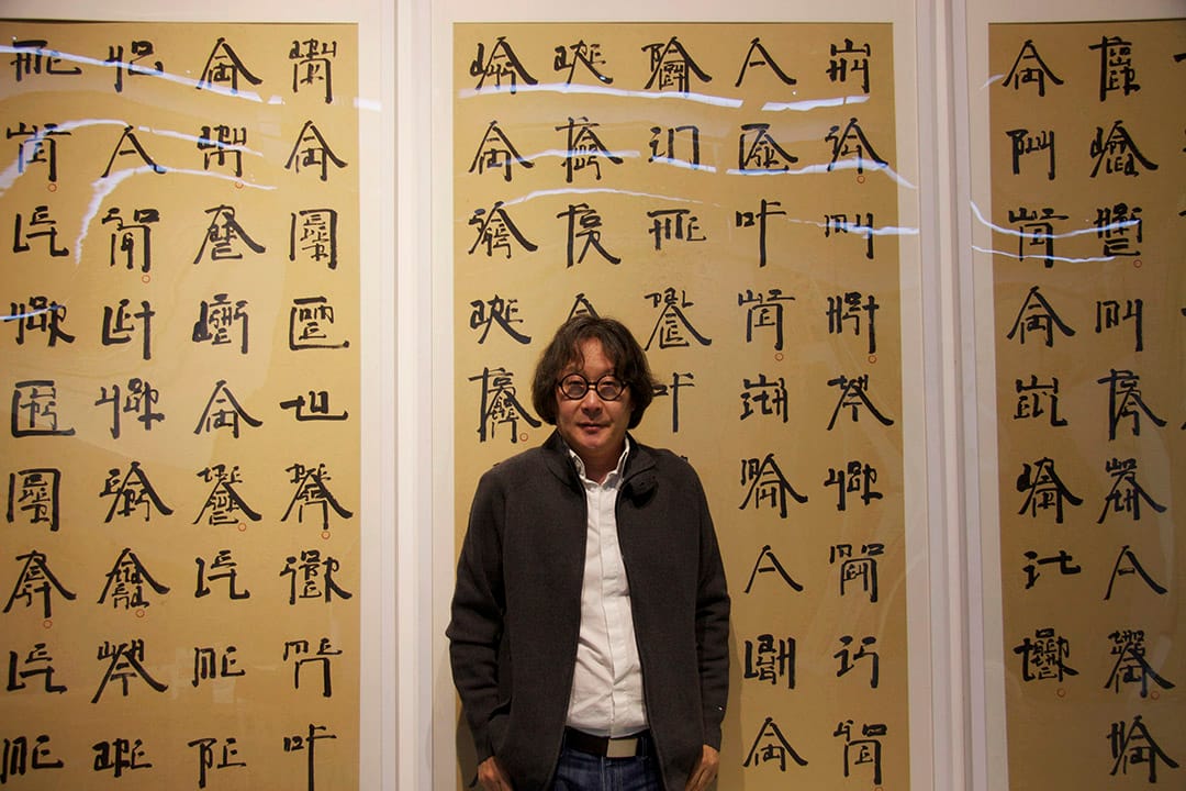 徐冰，背景是藝術家創作的《英文方塊字書法》。攝：阿 Lo