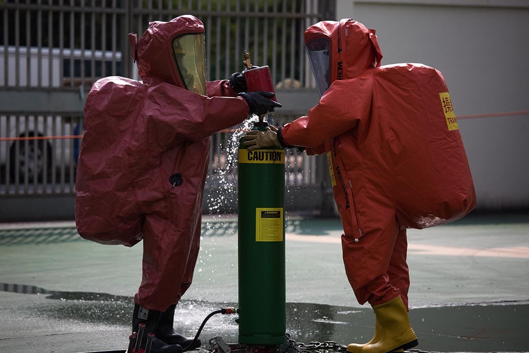 兩名穿著 EVO 化學保護袍的消防人員正在進行模擬處理氯氣洩漏事故的工作。攝：盧翊銘/端傳媒