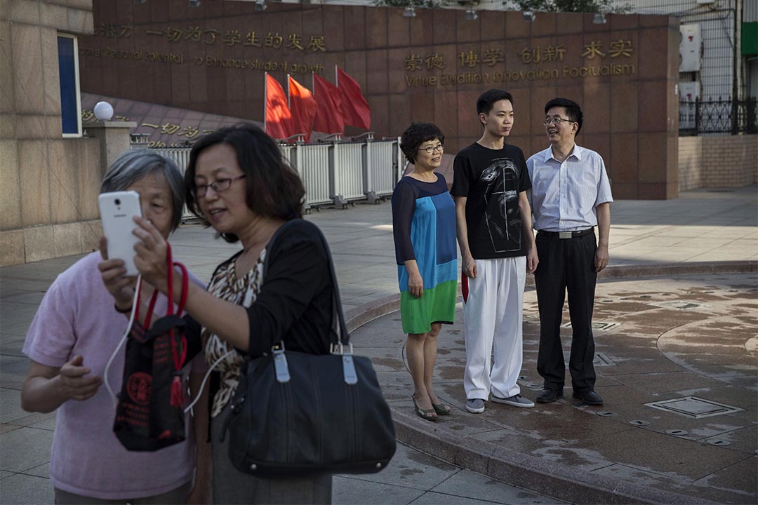 图为2016年6月8日，一个学生完成高考后与父母在一所学校门外合照。