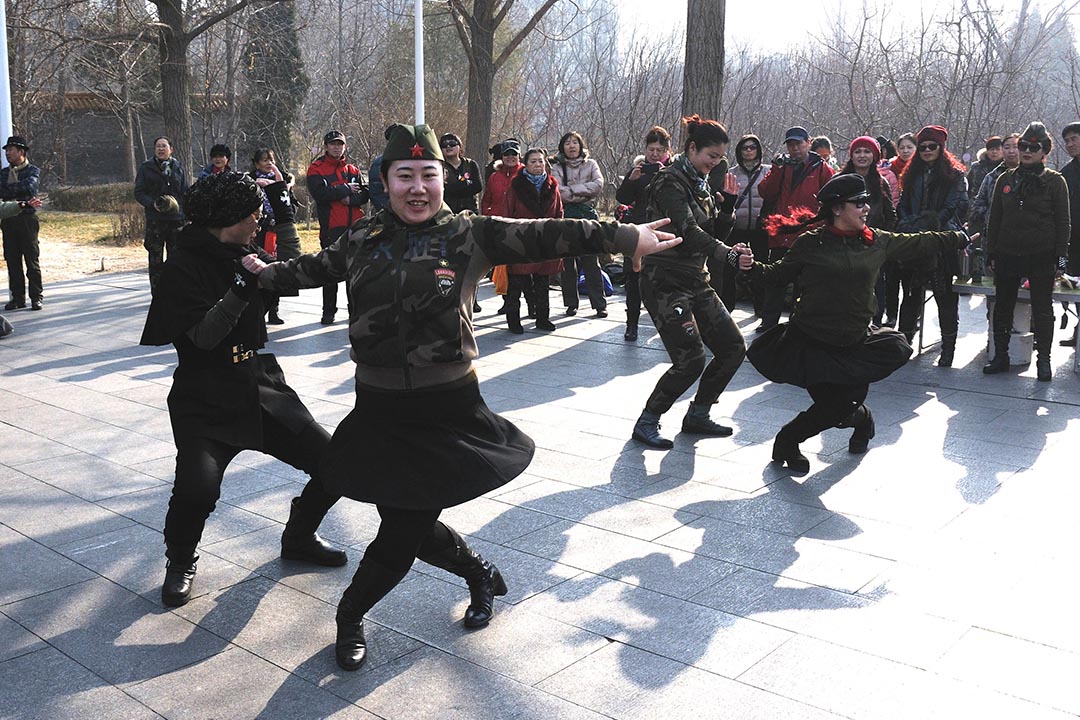 北京陶然亭公园，大妈们身穿迷彩制服，头戴贝雷军帽，尽情舞动展现风采。