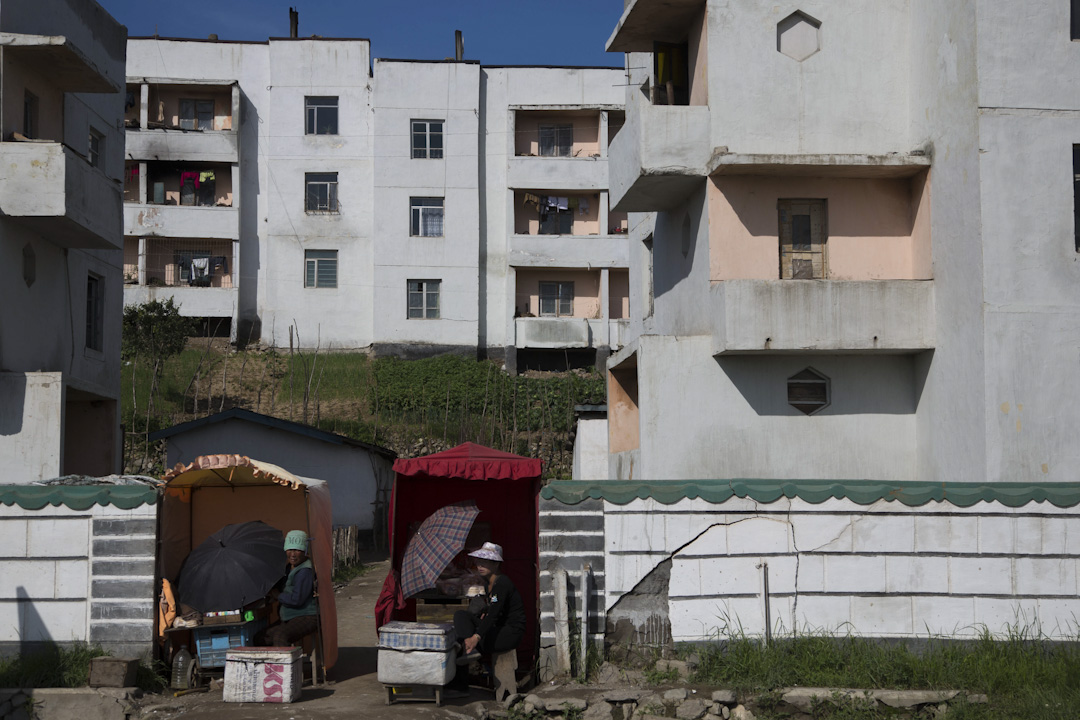 清津郊区，朝鲜妇女坐在一幢住宅前的小卖车摆卖。