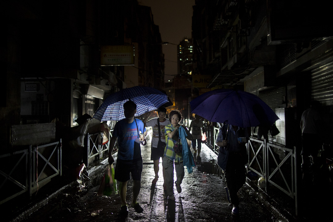 入夜後，澳門的街道仍然漆黑，還下起雨來，市民撐著傘，靠走過的車輛的車頭燈照明，橫越街道。