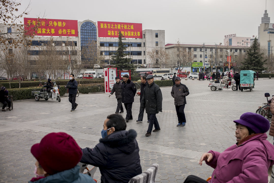 市民在雄县政府大楼前的广场消磨时间，背后有设立河北雄安新区的大字标语。