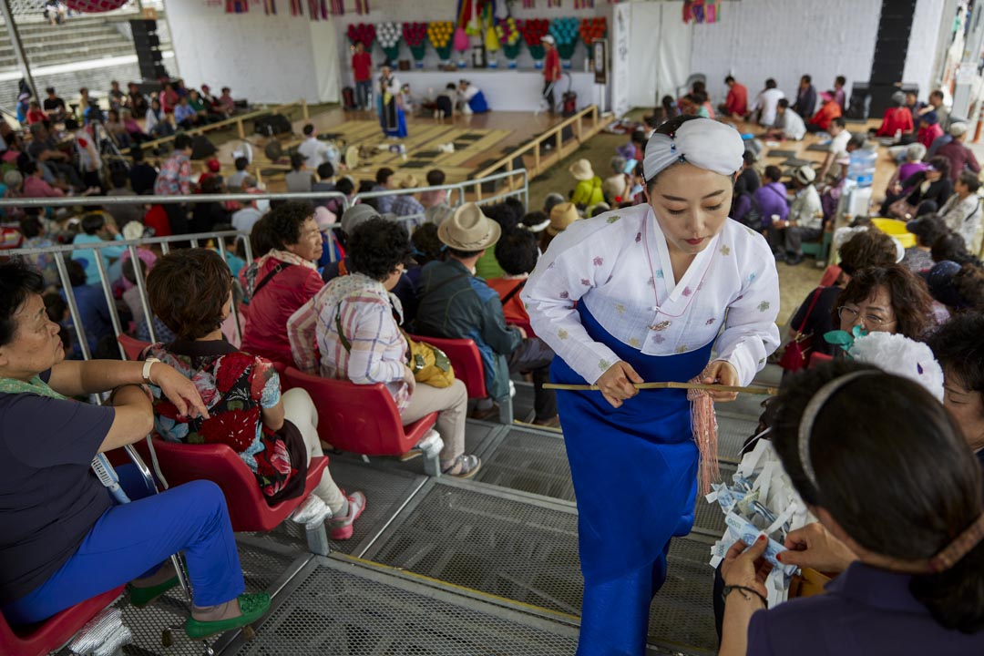 韩国江陵市，端午祭中一名年轻的萨满巫师正在收集捐款。长达一个多月的端午祭为江陵市市民向山神祈求年年丰收的传统习俗，于2005年成功向联合国教科文组织将端午祭申报为非物质文化遗产。