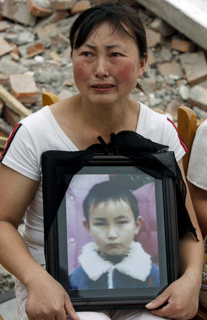 2008年5月22日，四川地震后富新二小的废墟上，刘孟瑛捧着儿子的遗照。