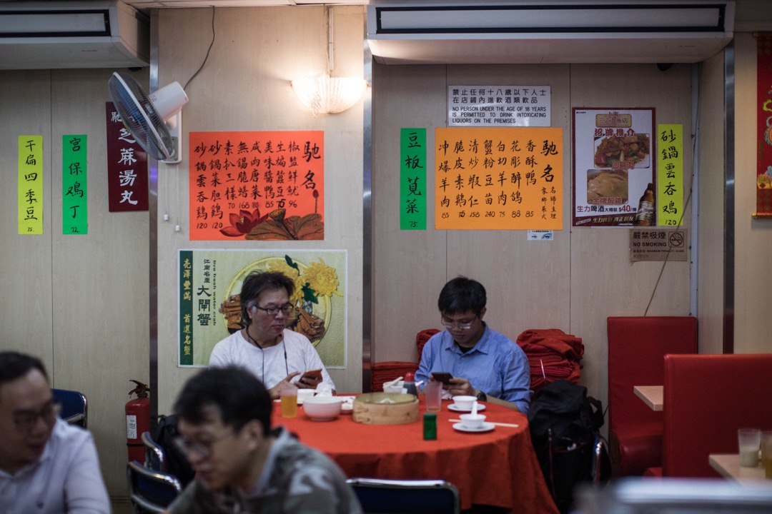 饭店的伙计将每张圆枱面的桌子铺上大红色的桌布，和红色的卡座沙发看上去很配套。墙壁上贴满了彩纸，上面是毛笔字写的菜单。