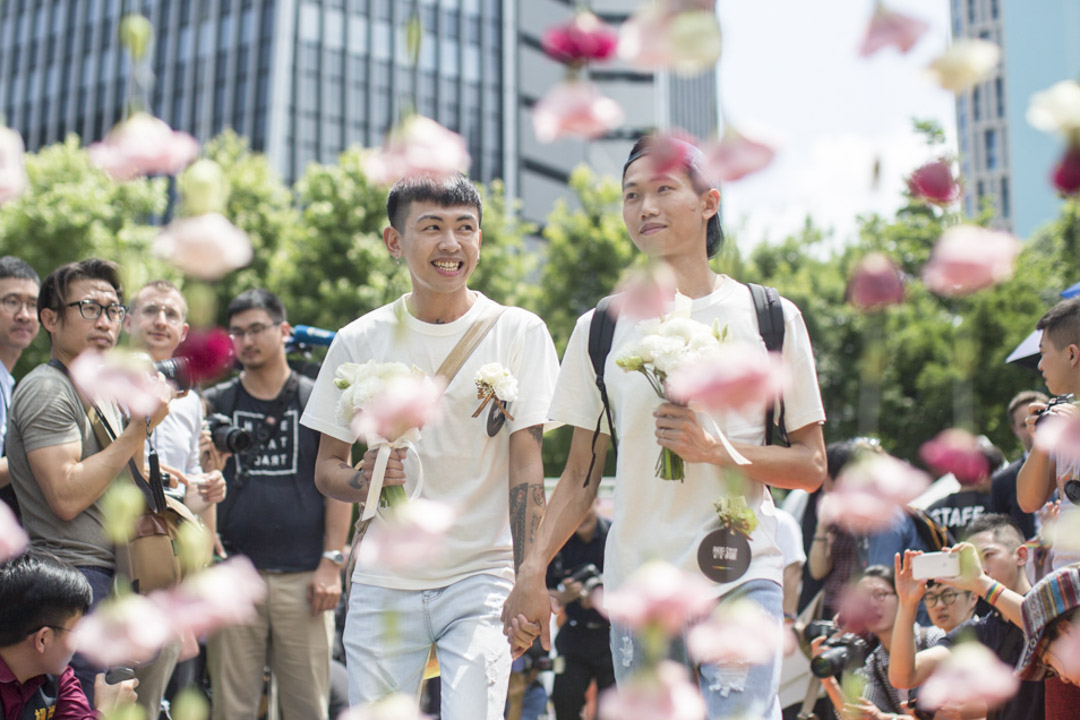 完成结婚登记的同志伴侣穿越幸福拱门踏上彩虹地毯，接受祝贺。