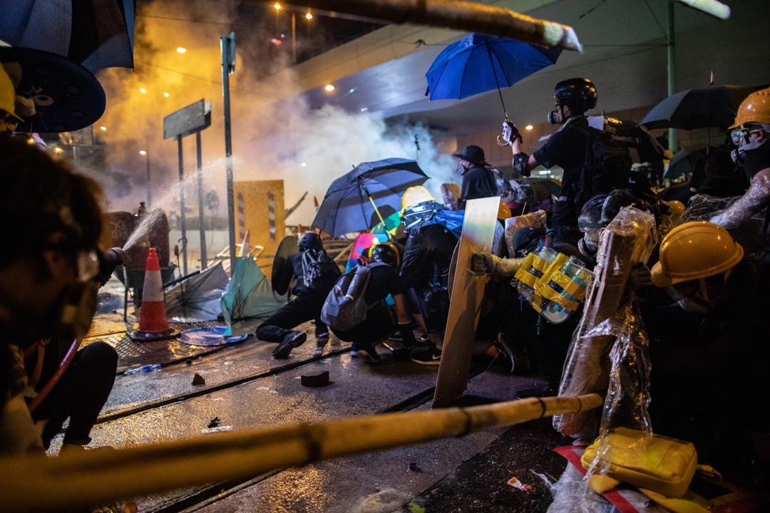 示威者以雨伞和消防喉作掩护，预备抵挡警察下一波的催泪弹。