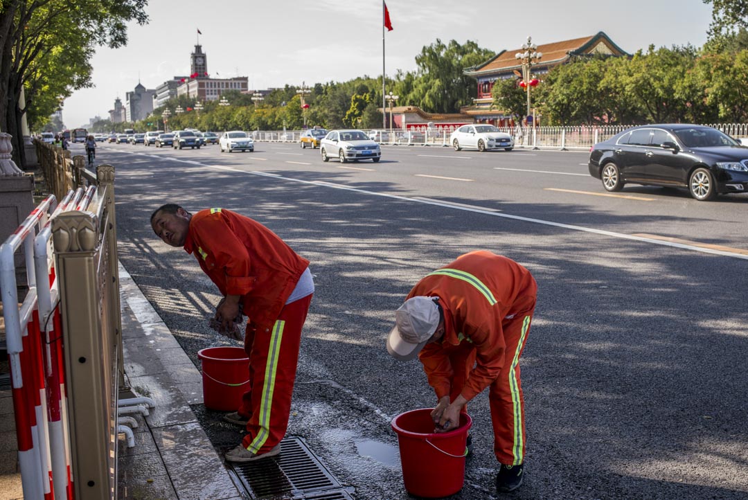 街上有工人提着水桶，擦着街邊金屬色的路障欄。