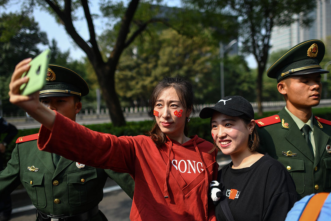 北京街头，脸上贴著红色贴纸的市民在解放军身旁自拍合影。