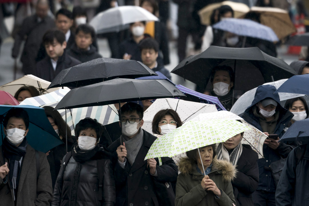 2020年2月13日，東京，戴著口罩的市民拿著傘步行在路上。