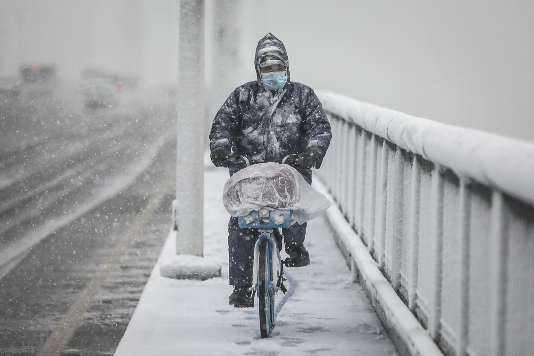 2020年2月15日，武汉大雪，一个戴著口罩的人骑著单车穿过大桥。