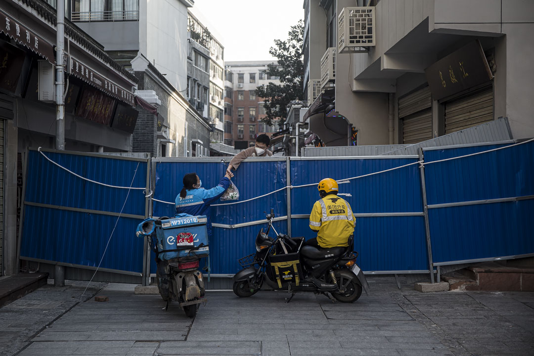 武汉户部巷社区，送餐员将外卖递给围栏内的居⺠。