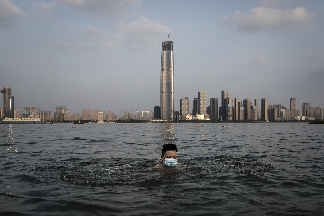 2020年6月30日在中国武汉，一个戴著口罩的男孩在被洪水淹没的公园里游泳。 