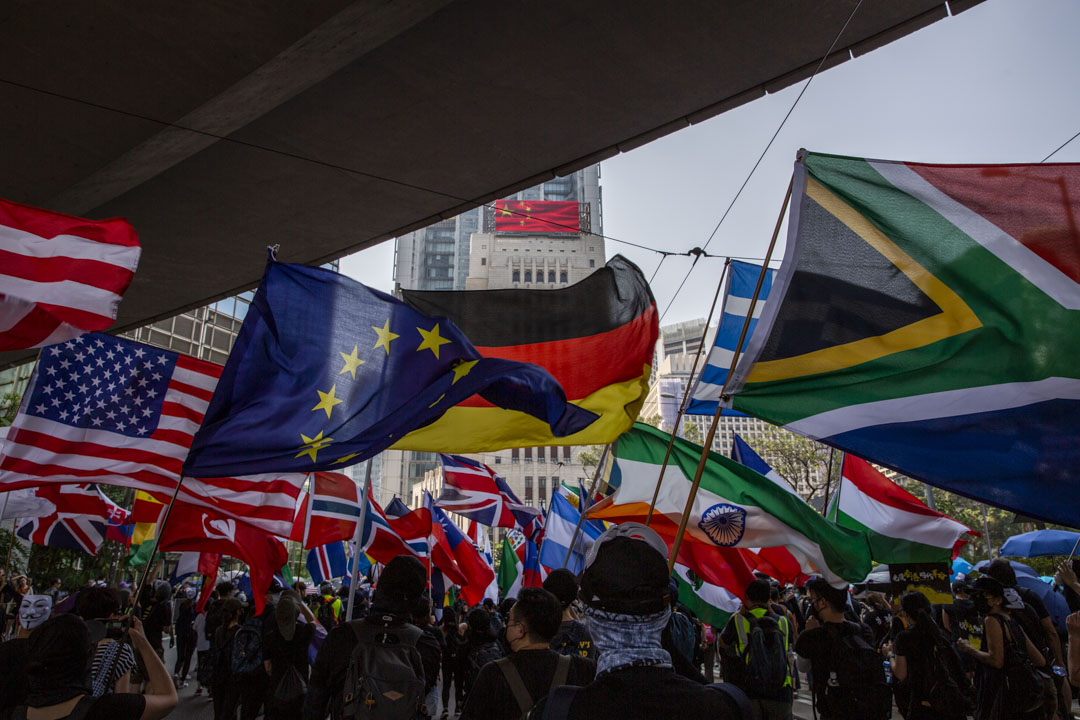 2019年10月1日，港岛有游行，参加者手持多国国旗途经中国银行大厦。