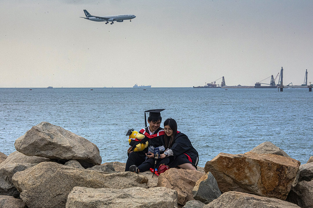 2020年11月30日香港国际机场外，一架国泰航空飞机降落，一对情侣拍毕业照。