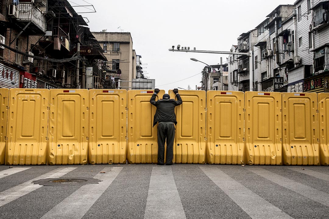 2020年3月8日，封城中的武漢，一個戴著口罩的男士隔著圍板與住宅區內的人交談。