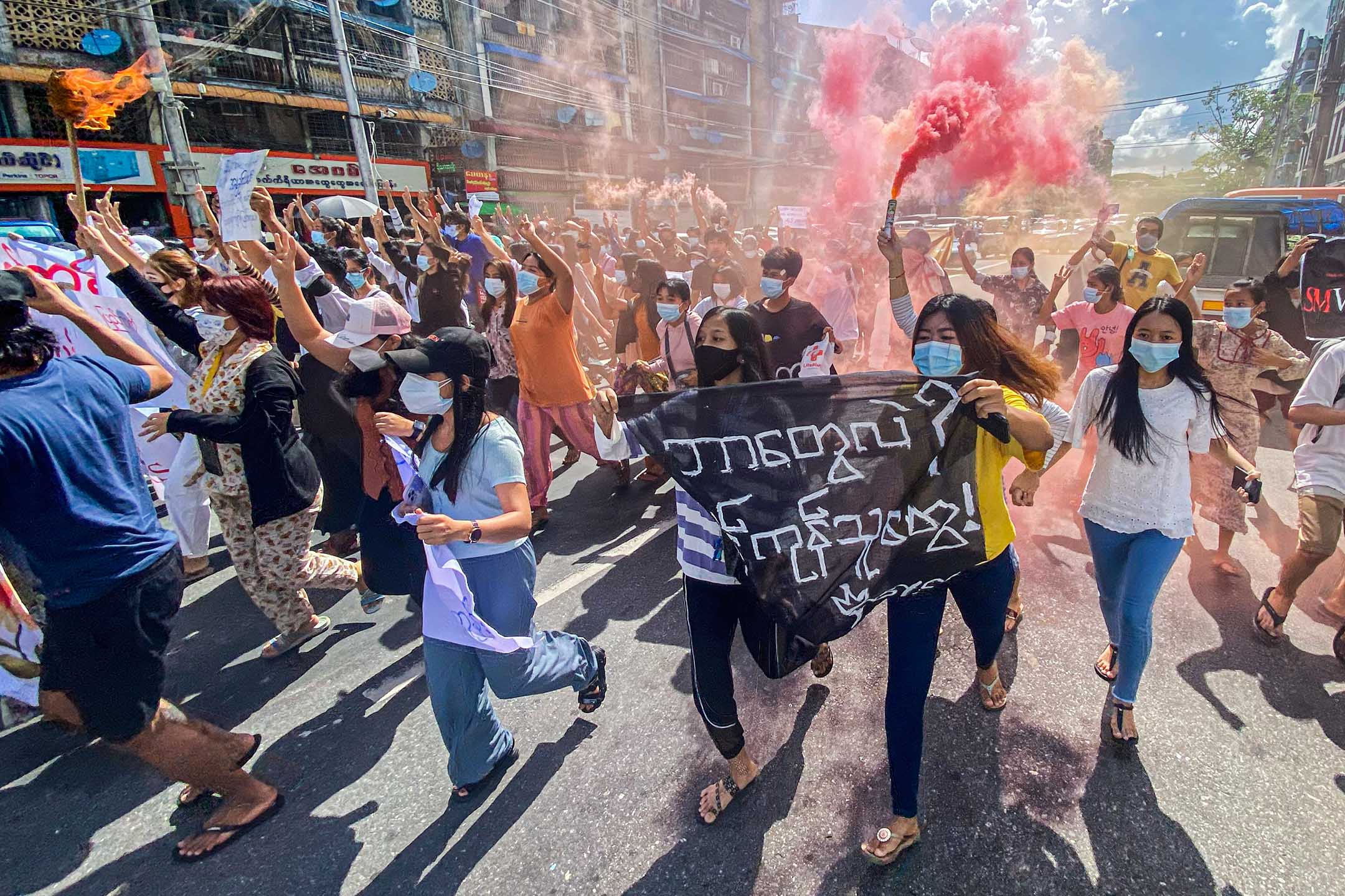  2021年7月14日缅甸仰光，反政变示威游行期间，妇女手持横幅和紧急信号棒奔跑。