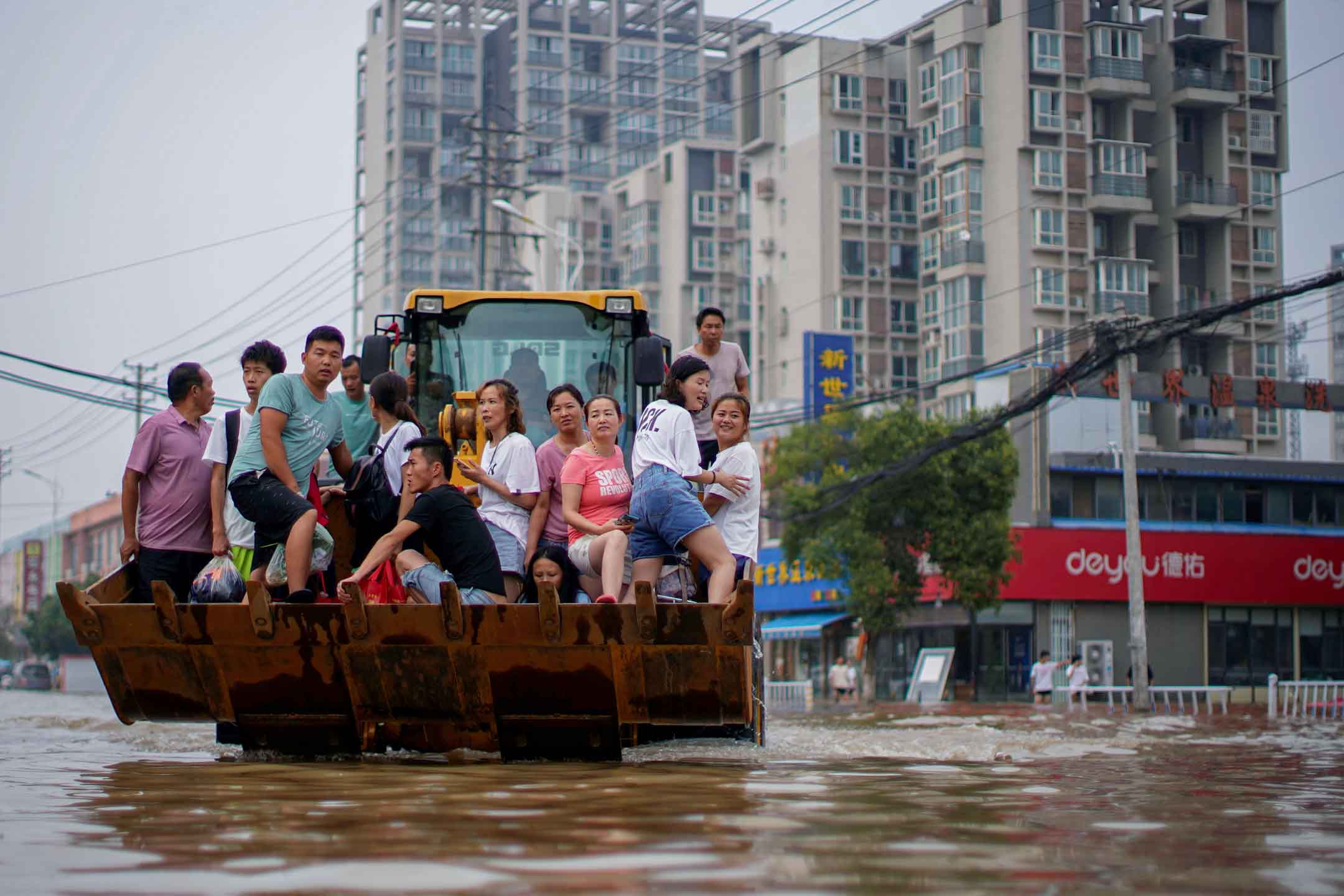 2021年7月23日中国河南省郑州市，人们骑着装载机穿过洪水。